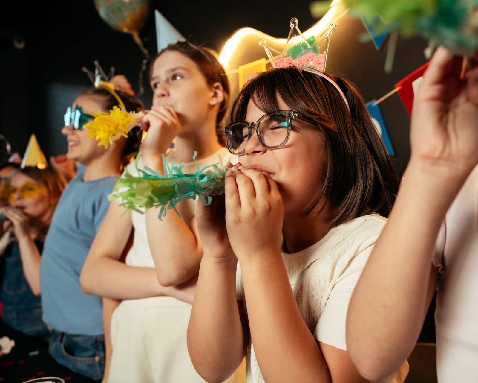 Teens in party hats blowing horns at a birthday at Bond's