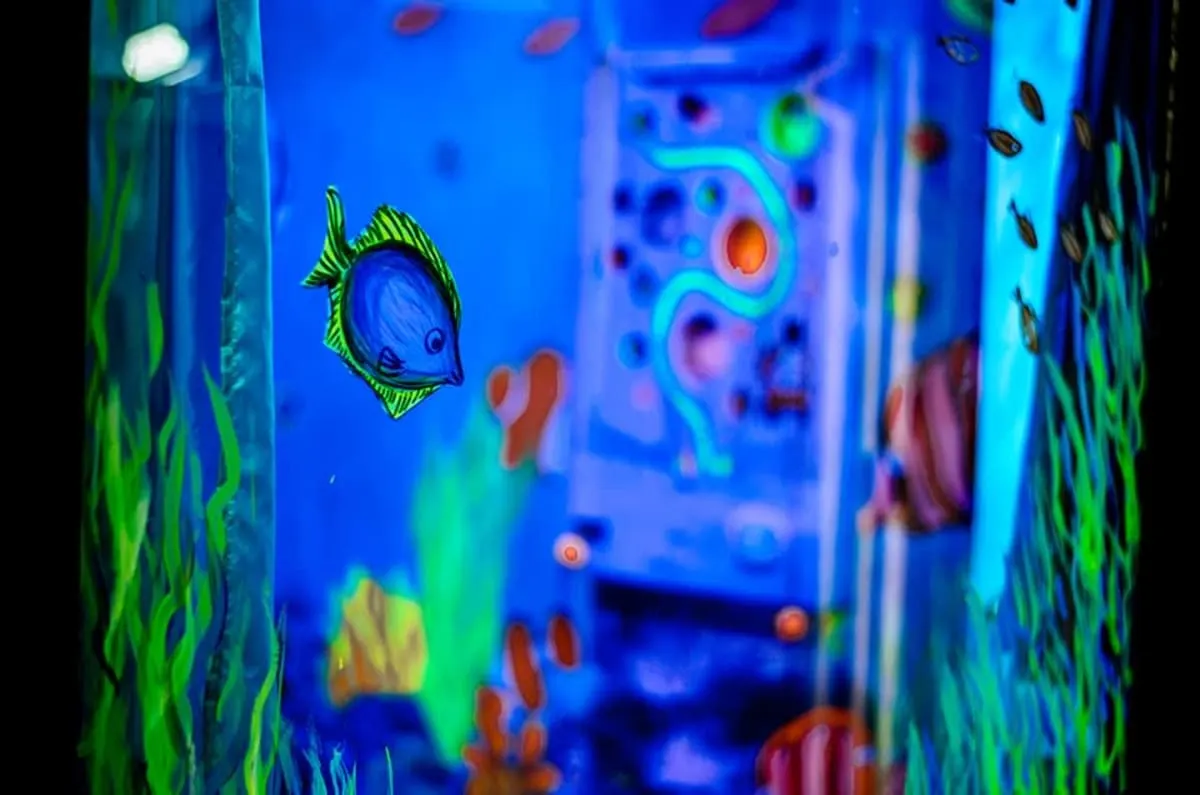 A glowing underwater mural of tropical fish and seaweed beside a wall panel with a winding neon maze puzzle