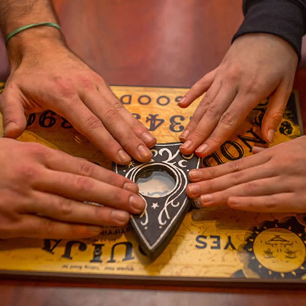 Four hands resting on the planchette of a Ouija board on a wooden table