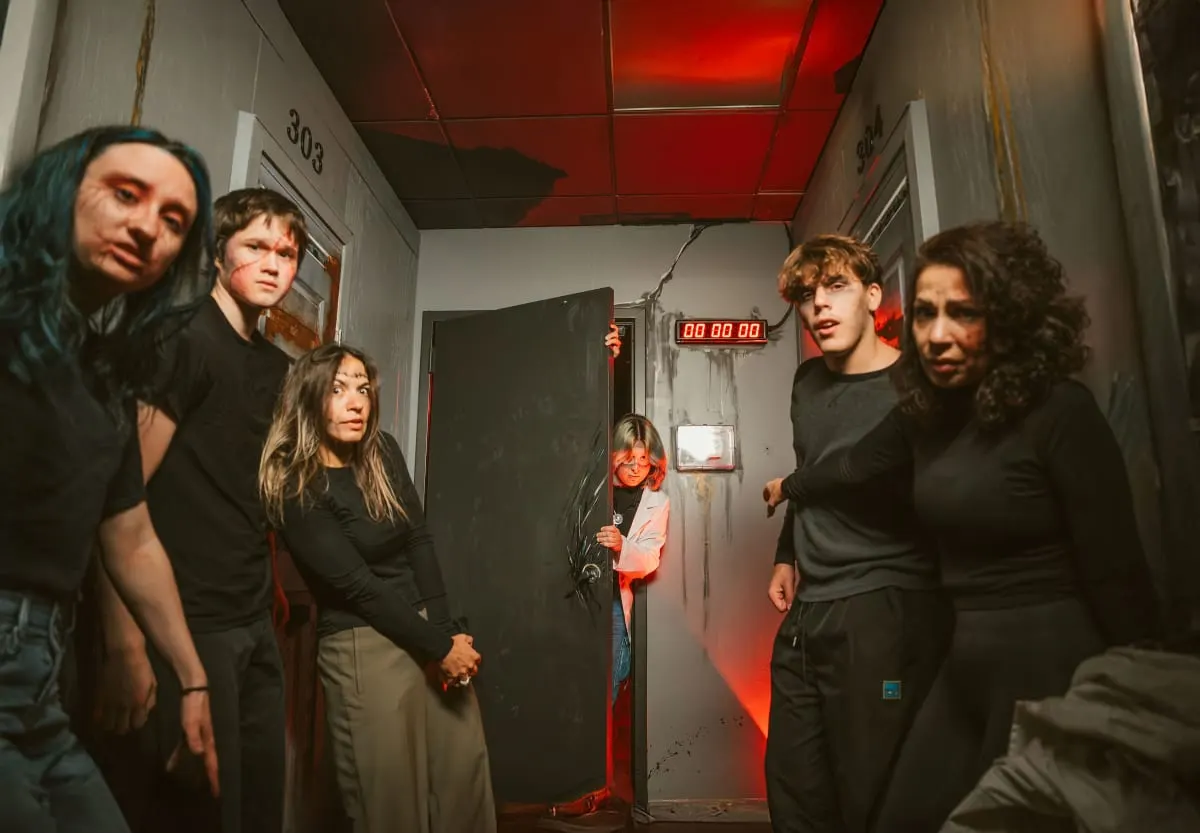 A group of players bunched in a narrow asylum corridor lit red, beside a door marked 303 and a red digital countdown