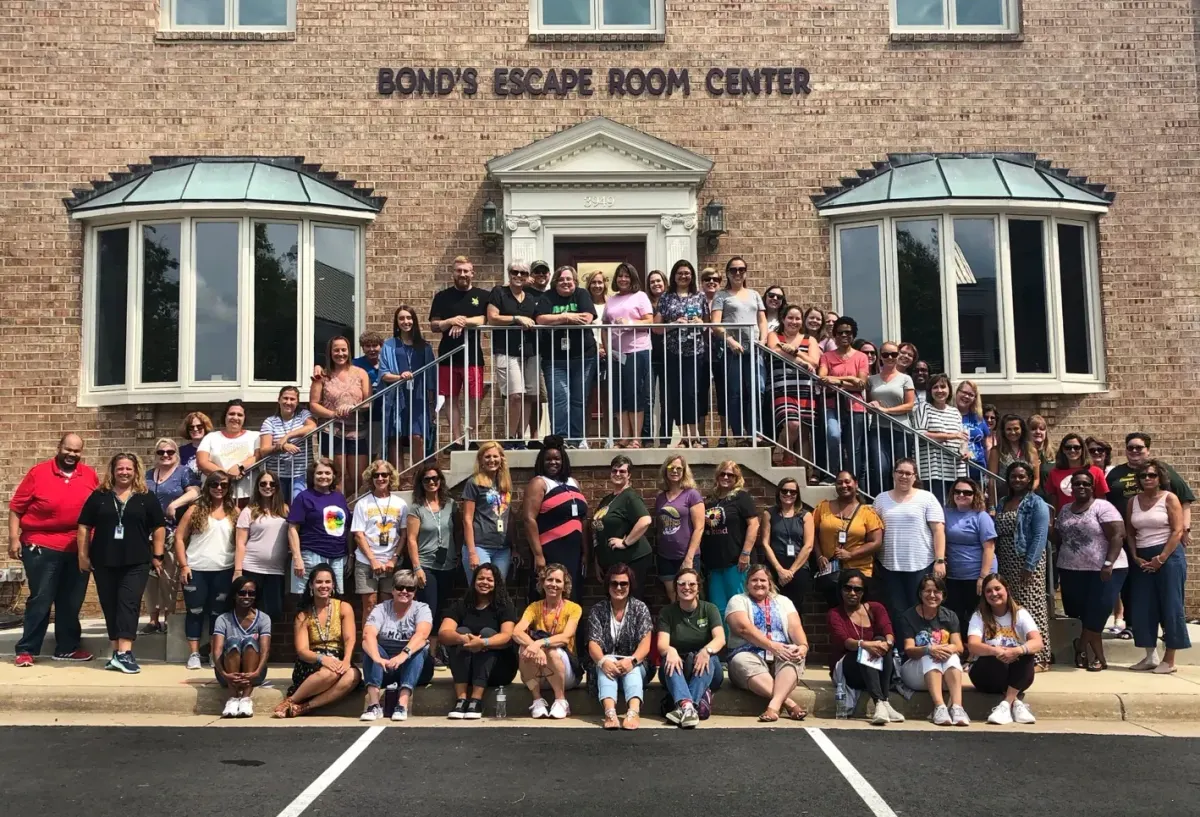 Dozens of school staff in casual clothes posing on the front steps and railings of Bond's Escape Room Center at 3949 University Drive in Fairfax