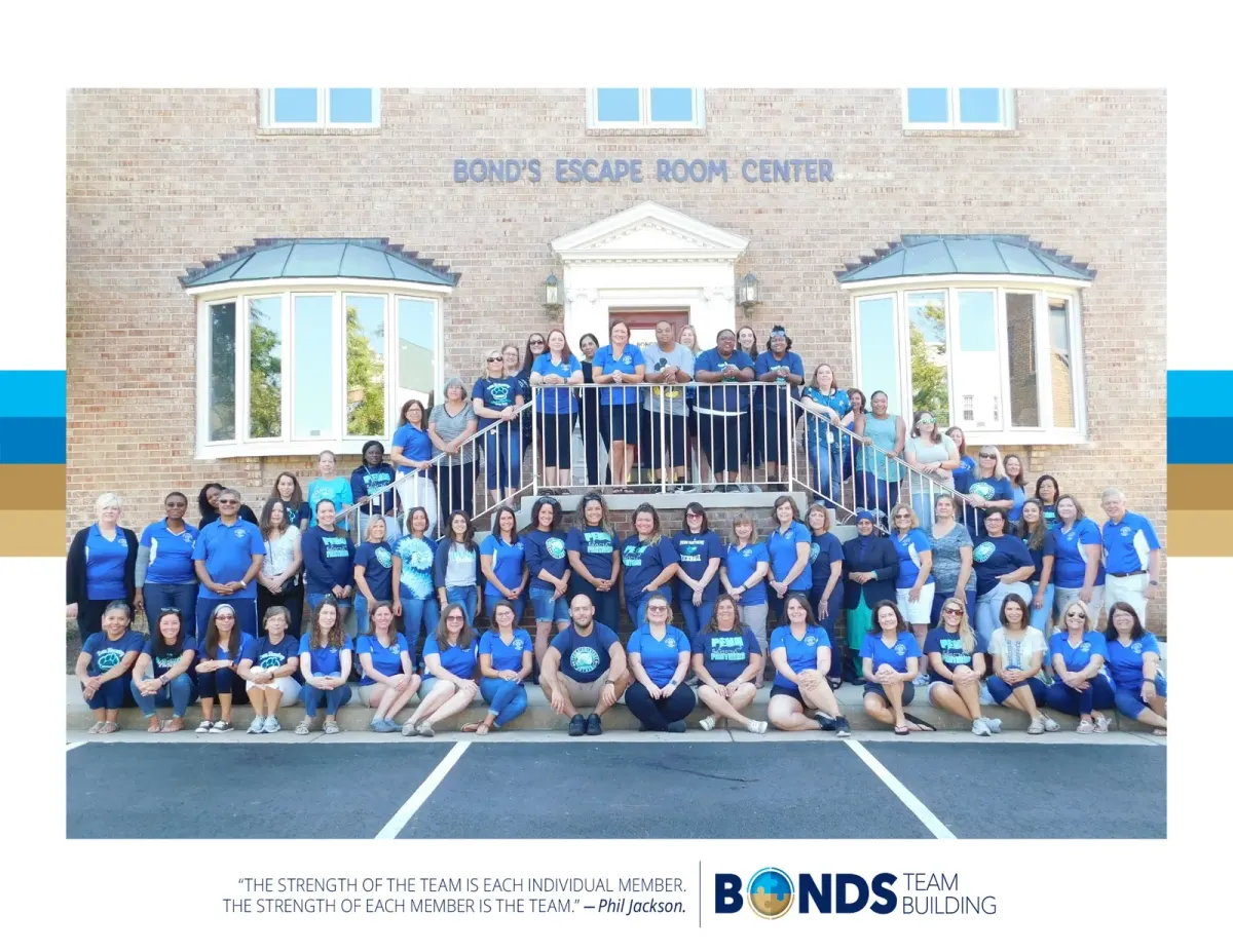 Dozens of school staff in matching blue shirts posing on the front steps of Bond's Escape Room Center in Fairfax