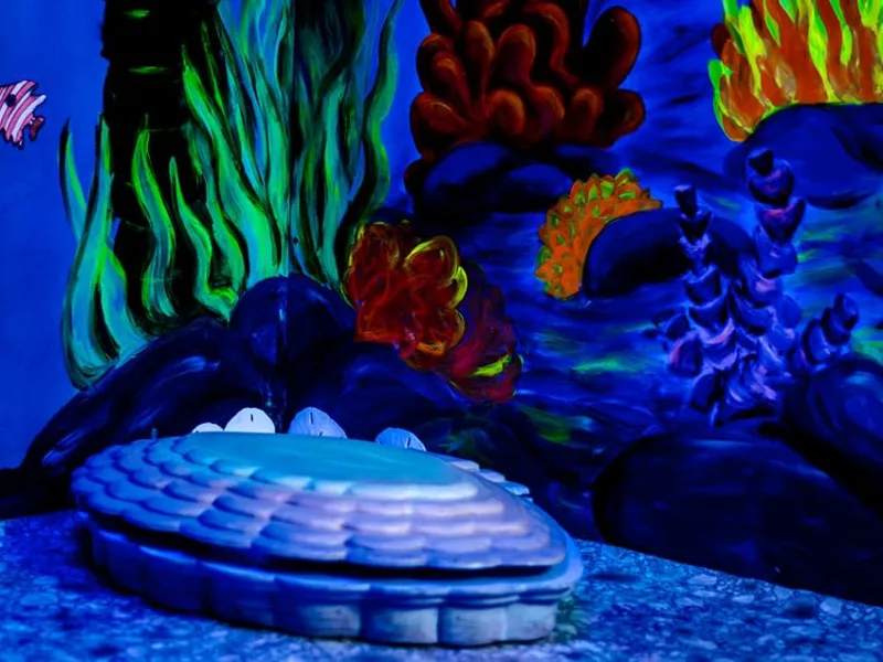 A painted reef and a giant clam shell glowing under blacklight inside Bowl Voyage at Bond’s Fairfax