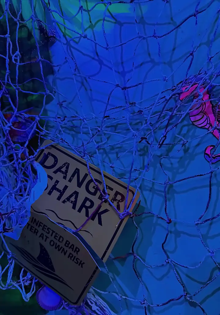 A fishing net hung with a “Danger: Shark” sign and a seahorse under blue light inside Bowl Voyage: Blood Bowl