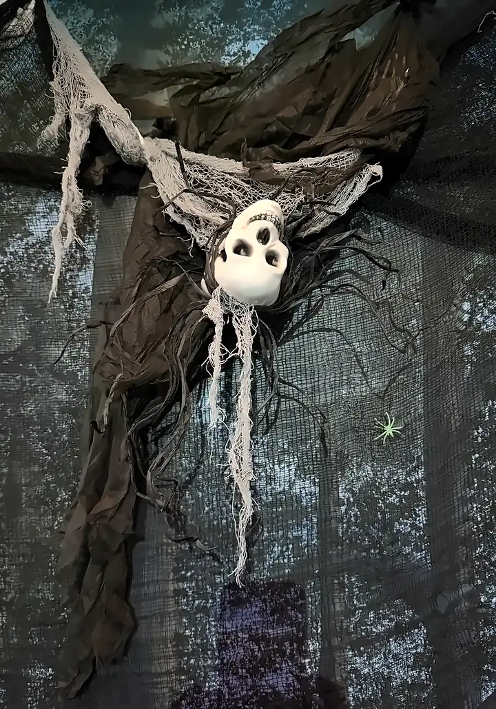 A skull in black gauze and cobwebs hangs against the painted forest backdrop