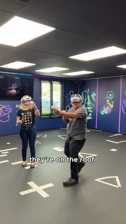 Two adults in VR headsets playing in the arena, with the caption "they're on the roof"